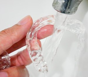 Patient rinsing clear aligner in sink