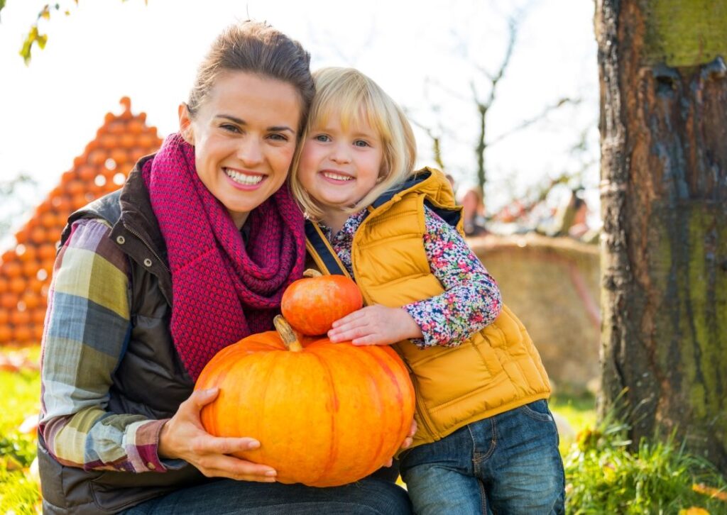 A woman and child holding pumpkins.