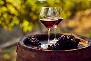 Two glasses of wine and some grapes sitting on a wine barrel 