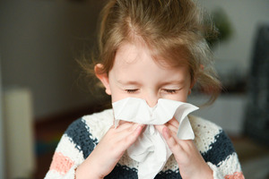 Little girl blowing her nose with a tissue